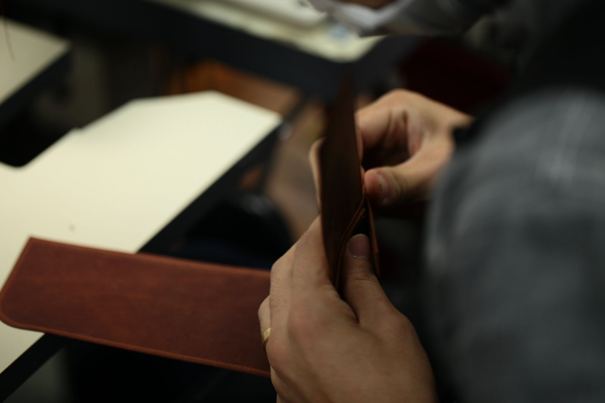 茶色の革パーツを両手で整える作業のクローズアップ。